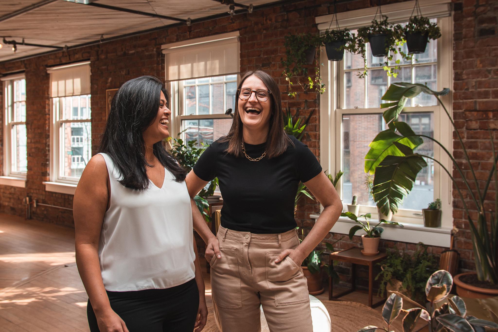 Wavy founders laughing in bright room with exposed bring and hanging plants.